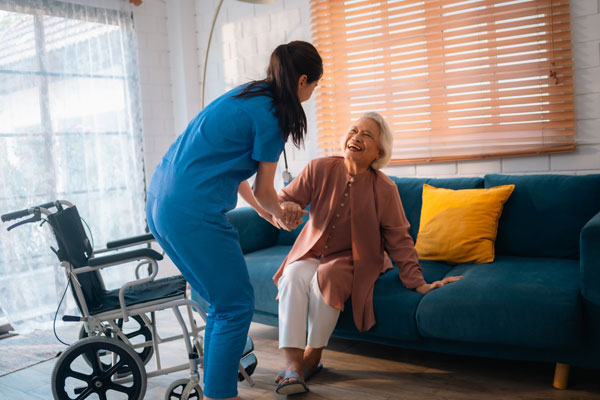 Nurse helping older woman from couch to wheelchair.