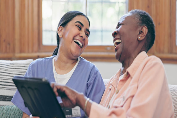 Caregiver with older adult using computer, both are laughing.