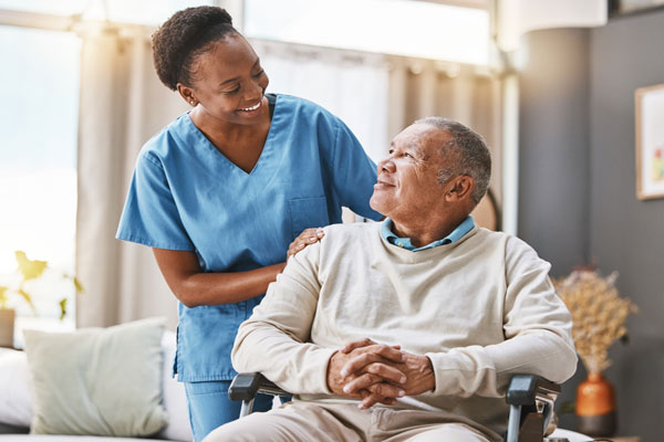 Smiling female caregiver helping smiling male older adult in a wheelchair.