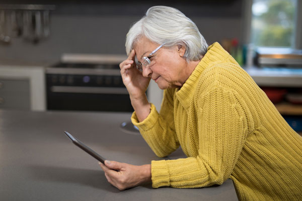 Concerned older adult looking at her computer tablet.