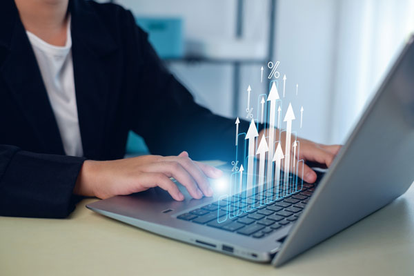 Businesswoman typing on laptop that shows up arrows rising above keyboard.