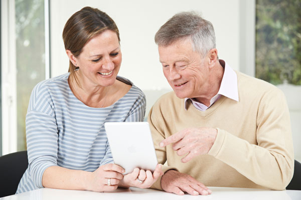 Older man and daughter looking at home care agencies on digital tablet.